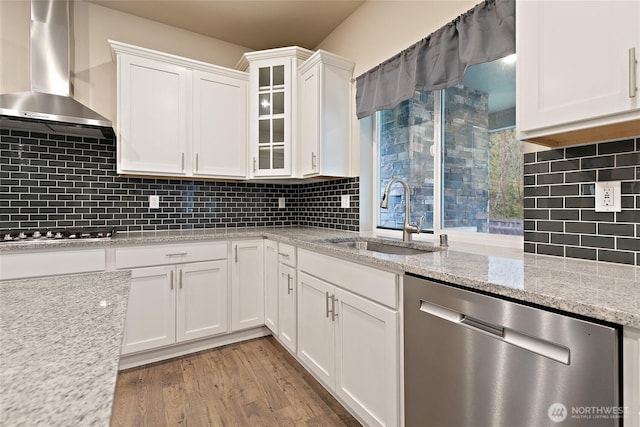 kitchen with a sink, wood finished floors, stainless steel appliances, white cabinets, and wall chimney range hood