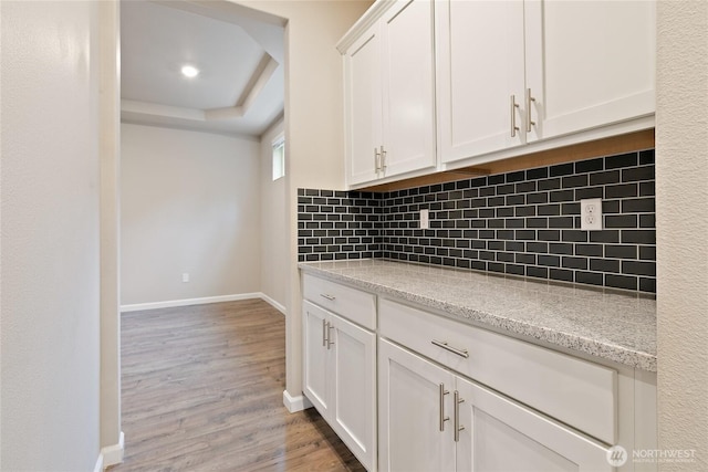 kitchen with baseboards, light wood finished floors, decorative backsplash, white cabinets, and a raised ceiling