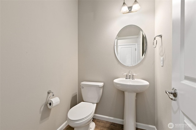 half bath with a sink, baseboards, toilet, and wood finished floors