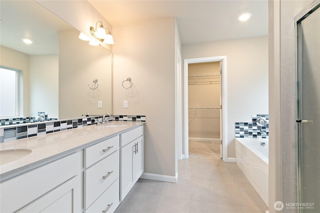 bathroom featuring a walk in closet, double vanity, backsplash, and a sink