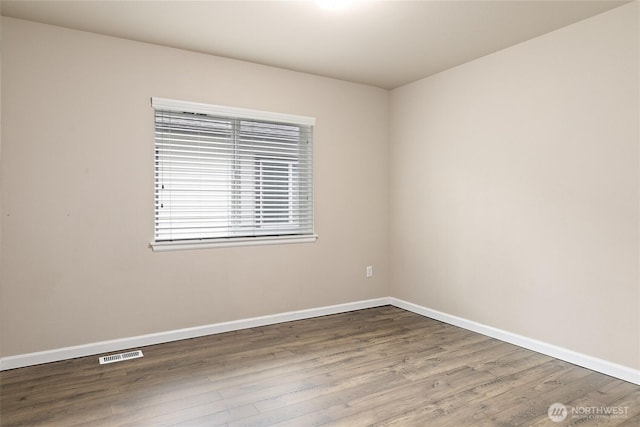 spare room with wood finished floors, visible vents, and baseboards