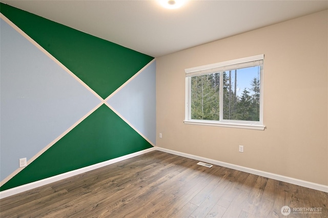 spare room featuring visible vents, baseboards, and wood finished floors