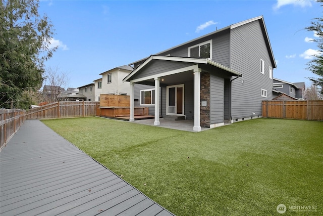 rear view of property featuring a deck, a patio area, a yard, and a fenced backyard