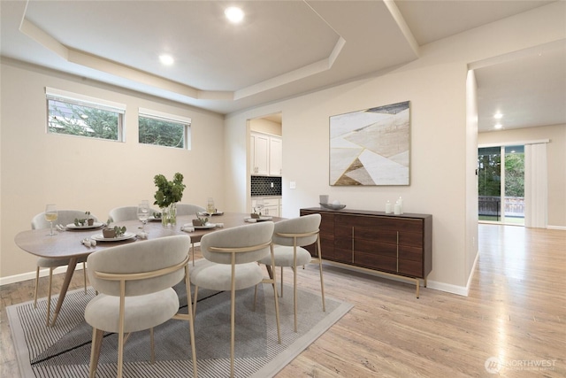 dining area with baseboards, light wood-type flooring, and a tray ceiling