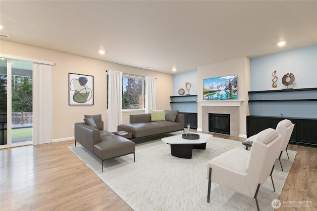 living room featuring light wood finished floors, a glass covered fireplace, recessed lighting, and a wealth of natural light