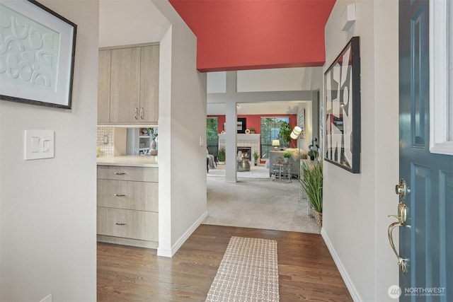 entrance foyer with a lit fireplace, dark wood-style flooring, and baseboards