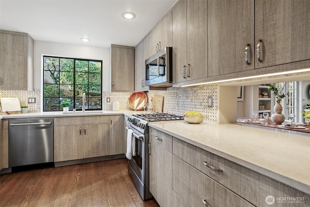 kitchen featuring dark wood-style floors, stainless steel appliances, tasteful backsplash, light countertops, and a sink