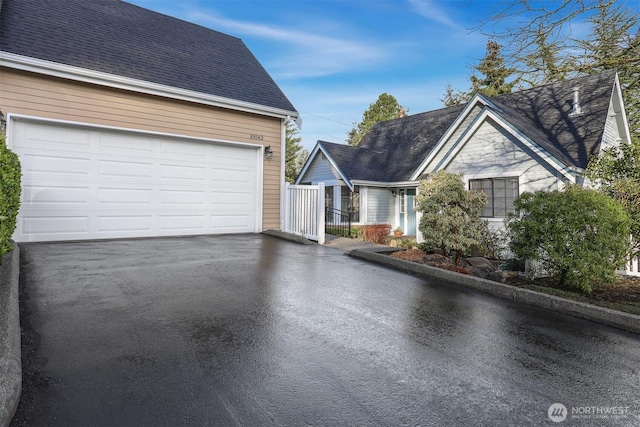 view of front facade featuring aphalt driveway, a shingled roof, and a garage