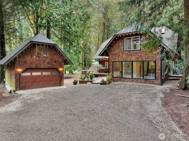 view of front of property with a detached garage, an outbuilding, a view of trees, and roof with shingles