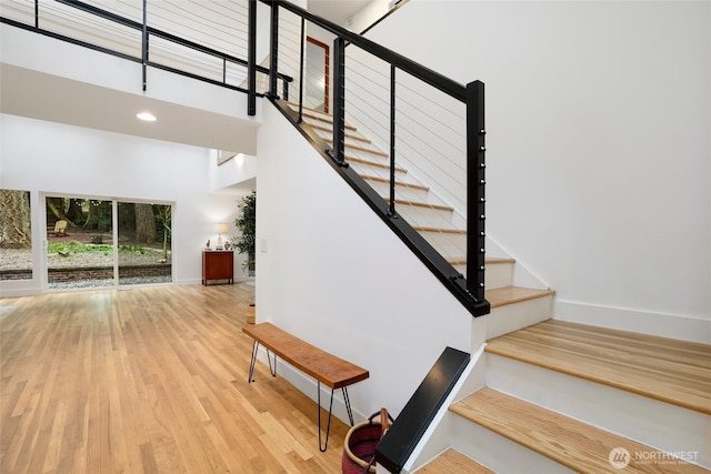 staircase with recessed lighting, baseboards, wood finished floors, and a towering ceiling