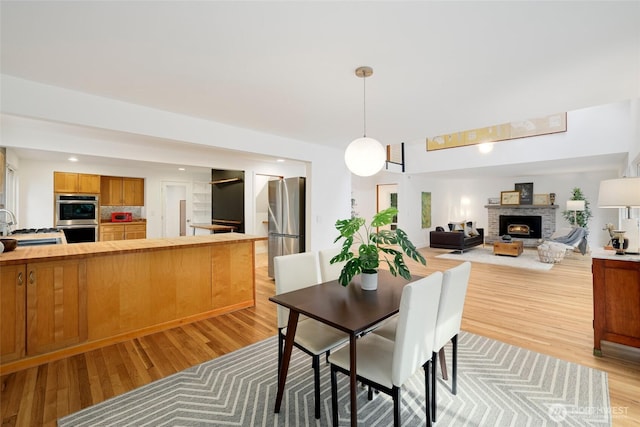 dining room featuring light wood-style flooring, recessed lighting, and a warm lit fireplace