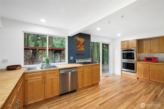 kitchen with tasteful backsplash, butcher block counters, light wood-type flooring, stainless steel appliances, and a sink