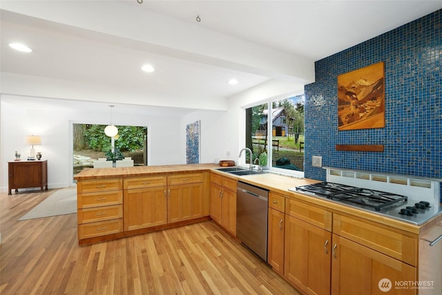 kitchen featuring a peninsula, stovetop, a sink, dishwasher, and light wood-type flooring