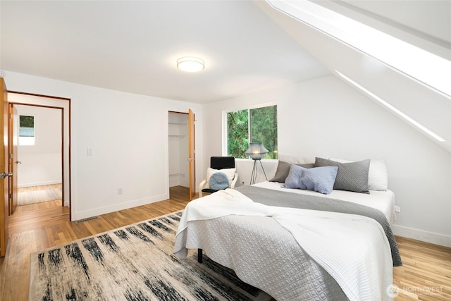 bedroom with visible vents, baseboards, light wood-type flooring, and vaulted ceiling