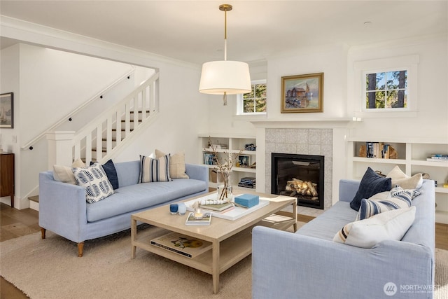 living room featuring stairway, wood finished floors, a tiled fireplace, and crown molding