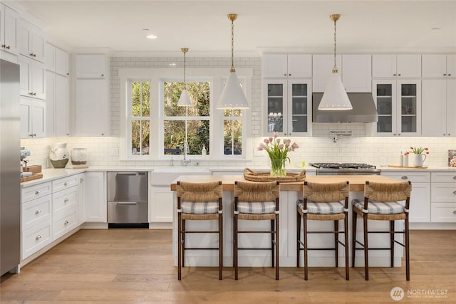 kitchen with a kitchen island, light wood-type flooring, stainless steel appliances, exhaust hood, and white cabinetry