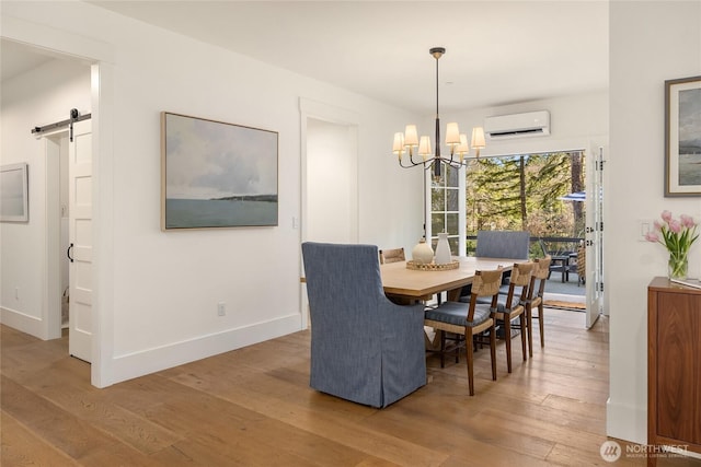 dining room featuring wood finished floors, baseboards, a wall mounted AC, a barn door, and a notable chandelier