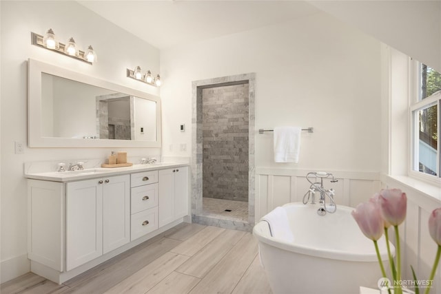 bathroom featuring a wainscoted wall, a freestanding tub, a sink, a tile shower, and double vanity