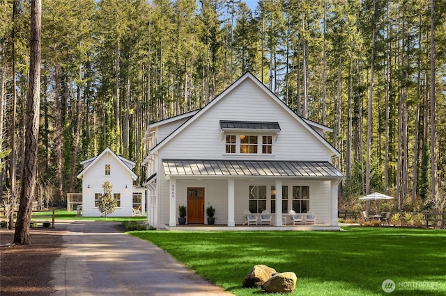 view of front of property featuring a front lawn, a standing seam roof, a forest view, covered porch, and metal roof