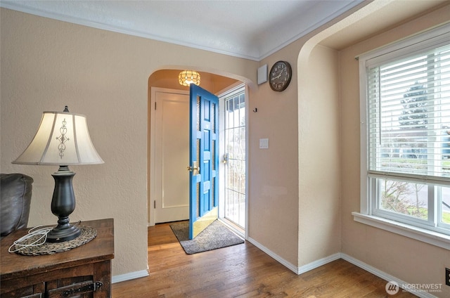 entrance foyer with baseboards, arched walkways, wood finished floors, and a textured wall