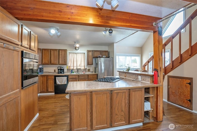 kitchen with light countertops, appliances with stainless steel finishes, wood finished floors, brown cabinetry, and a sink