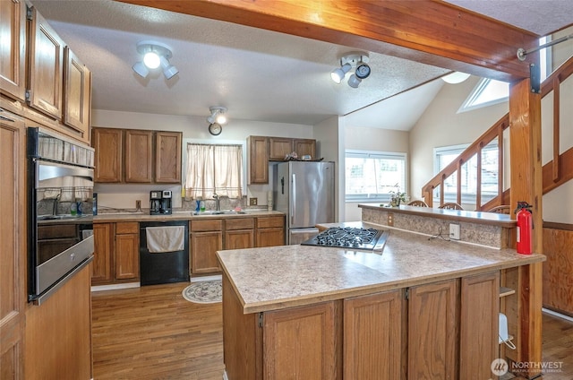 kitchen featuring light wood-style flooring, vaulted ceiling with beams, a sink, stainless steel appliances, and brown cabinets