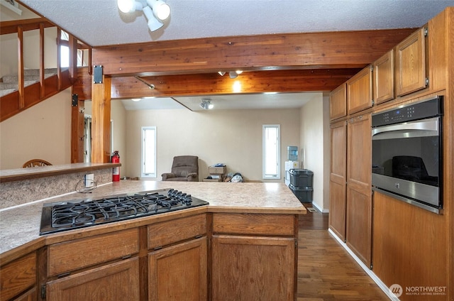 kitchen featuring open floor plan, light countertops, stainless steel oven, black gas stovetop, and dark wood-style floors