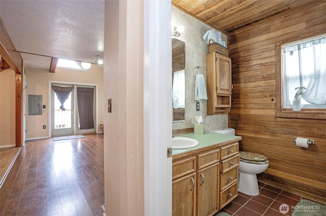 bathroom featuring vanity, wooden walls, wood finished floors, electric panel, and toilet