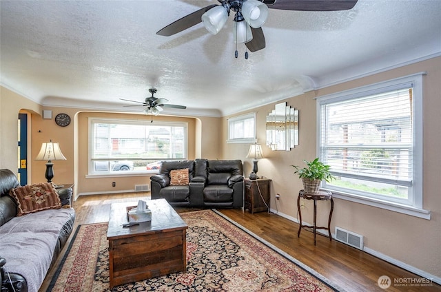 living room featuring arched walkways, visible vents, a textured ceiling, and wood finished floors