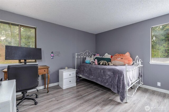 bedroom with light wood finished floors, a textured ceiling, and baseboards