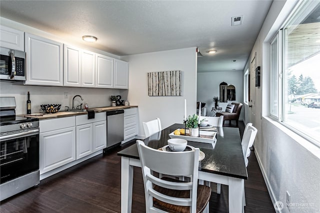 kitchen featuring dark wood-style flooring, stainless steel appliances, visible vents, white cabinetry, and a sink