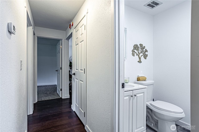 bathroom featuring visible vents, a textured wall, toilet, wood finished floors, and vanity