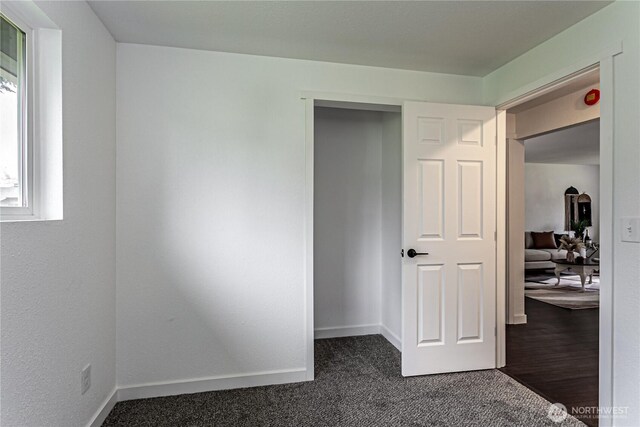 unfurnished bedroom featuring dark carpet and baseboards