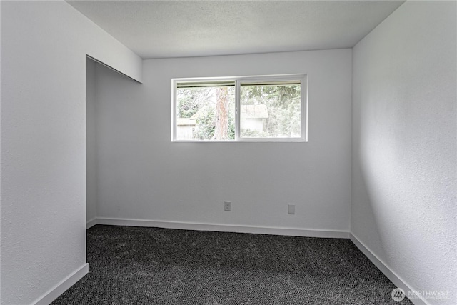 spare room with baseboards, dark carpet, and a textured ceiling