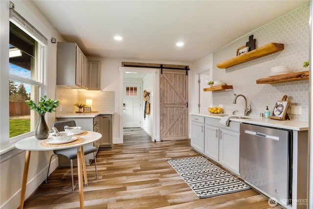 kitchen featuring open shelves, a sink, stainless steel dishwasher, a barn door, and light wood-style floors