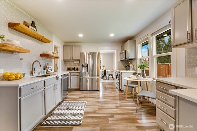 kitchen with open shelves, gray cabinets, light countertops, light wood-style floors, and appliances with stainless steel finishes