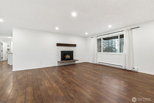 unfurnished living room with dark wood finished floors, a textured ceiling, a fireplace, a baseboard heating unit, and recessed lighting