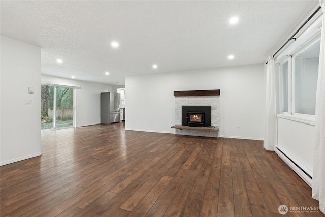 unfurnished living room featuring dark wood finished floors, a baseboard radiator, a textured ceiling, a brick fireplace, and recessed lighting