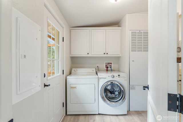 clothes washing area featuring separate washer and dryer, light wood-style flooring, and cabinet space