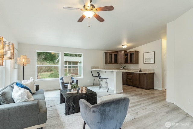 living area featuring baseboards, ceiling fan, light wood-style floors, and lofted ceiling