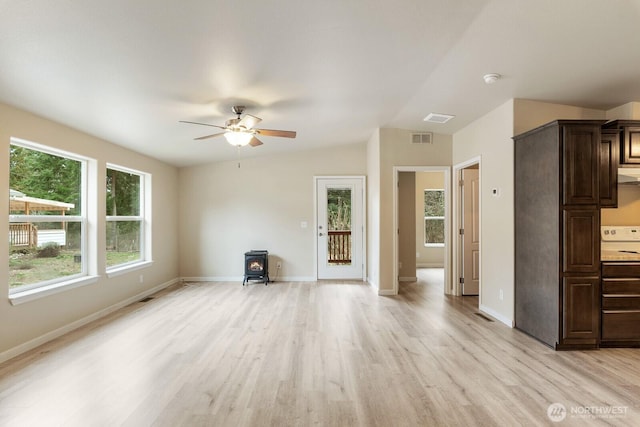 unfurnished living room with a ceiling fan, a wood stove, light wood-style floors, visible vents, and lofted ceiling