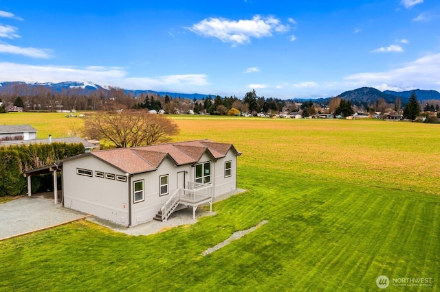 view of front facade featuring a mountain view, driveway, a front lawn, and roof with shingles