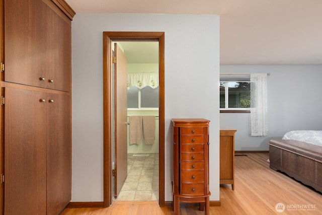 bedroom featuring light wood-style flooring, baseboards, and ensuite bathroom