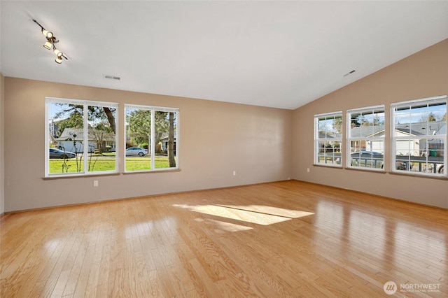 empty room featuring visible vents, wood-type flooring, lofted ceiling, and a healthy amount of sunlight