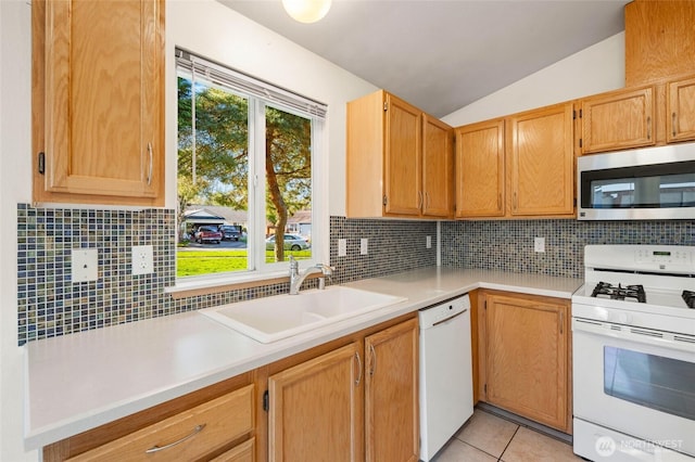 kitchen with a sink, white appliances, light countertops, light tile patterned floors, and vaulted ceiling