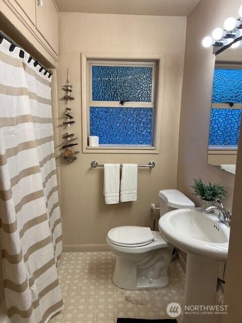 full bathroom with toilet, a shower with shower curtain, a sink, baseboards, and an inviting chandelier