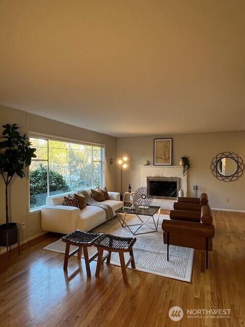 living area with a fireplace with raised hearth, baseboards, and wood finished floors