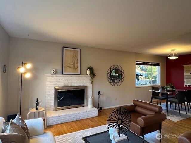 living room featuring a brick fireplace, baseboards, and wood finished floors