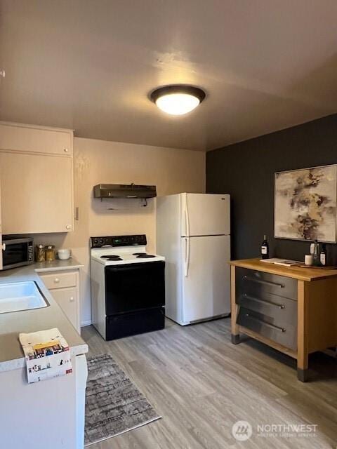 kitchen with stainless steel microwave, freestanding refrigerator, light countertops, a sink, and range with electric stovetop