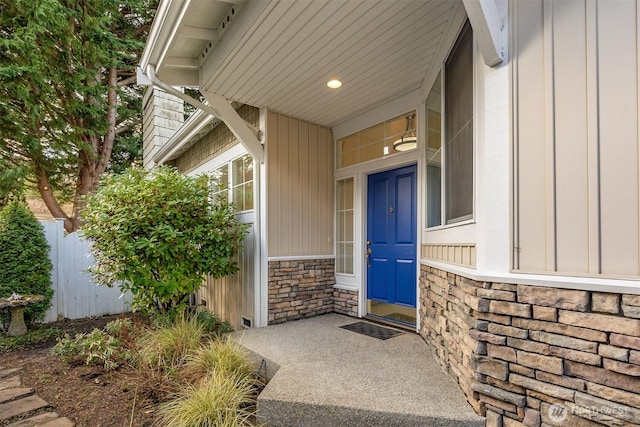 view of exterior entry featuring stone siding, board and batten siding, and fence